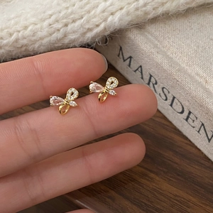 Gros plan de boucles d'oreilles nœud dorées avec zircons tenues entre les doigts