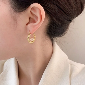 Elegant gold pearl hoop earrings with textured finish on model in white blazer