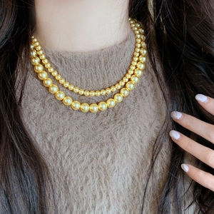 Élégant collier de perles double épaisseur doré champagne sur un pull en maille marron
