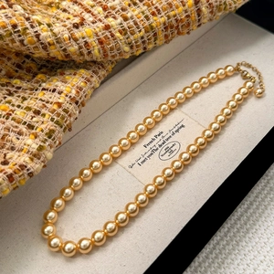 Détail d'un élégant collier de perles dorées avec fermoir mousqueton dans un écrin de luxe