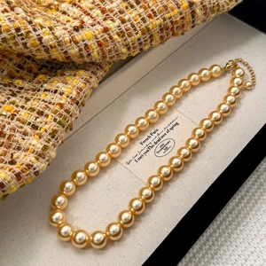 Détail d'un collier de perles champagne dorées avec fermoir sur tissu en tweed