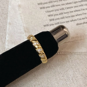Close-up of golden twisted rope ring with micro-pave zircons on a velvet stand