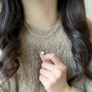 Double-layered gold necklace with white pearl beads and a heart-shaped shell pendant