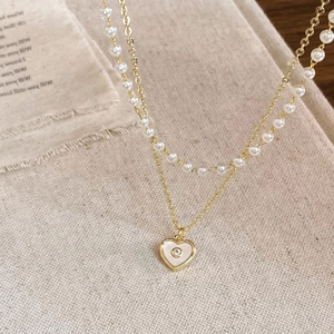 Detail of double-layer necklace featuring white pearls and heart-shaped shell pendant