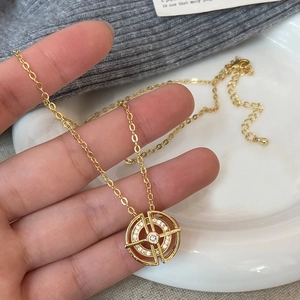 Élégant collier doré avec pendentif en zircone tenu sur un pull en maille grise