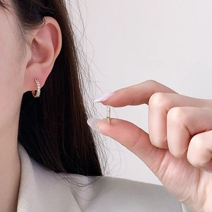 Gros plan de boucles d'oreilles huggies dorées avec zircons, portées et tenues en main