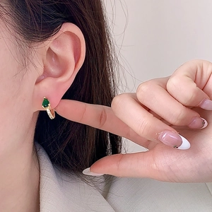 Boucles d'oreilles dorées avec zircon émeraude en forme de poire portées par un mannequin
