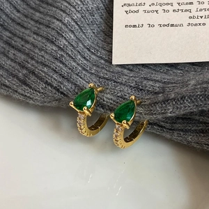 Gros plan de boucles d'oreilles dorées avec zircon poire vert émeraude sur tricot gris