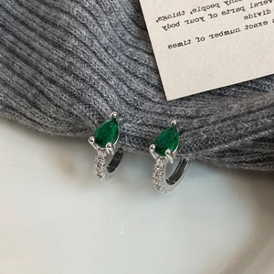 Détail de boucles d'oreilles créoles avec zircon émeraude sur un tissu texturé