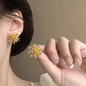 Golden dandelion starburst stud earrings with white zircons on a warm background