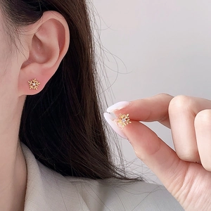 Nahaufnahme goldener Schneeflocken-Ohrstecker mit funkelndem Zirkon am Ohr