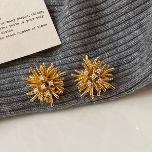 Macro detail of gold starburst earrings with sparkling zircon stones on textured fabric