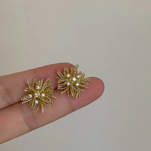 Close-up of a hand holding gold dandelion stud earrings with sparkling white zircons