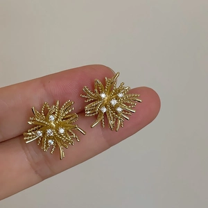 Detailed view of dandelion zircon earrings in warm gold finish held between fingers