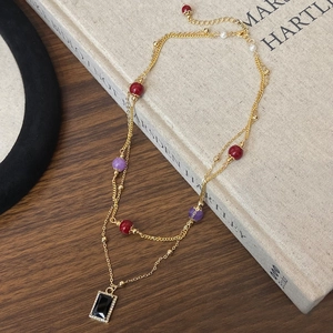 Detail of layered gold necklace with black stone pendant and colorful beads on books