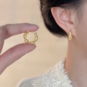 Vue macro des boucles d'oreilles créoles dorées torsadées au rendu chic sur l'oreille