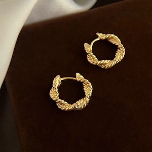 Détail de boucles d'oreilles créoles torsadées dorées avec texture en spirale et fini brillant