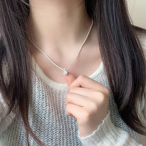 Minimalist silver chain necklace with round zircon pendant on model wearing white knit