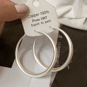 Macro detail of large matte silver circular hoop earrings made of 100% copper