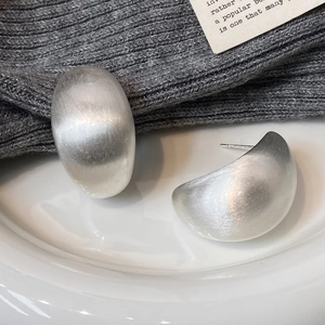 Close-up of matte silver brushed C-shape earrings on a white ceramic plate