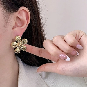 Détail de boucles d'oreilles fleurs dorées vintage avec texture martelée portée