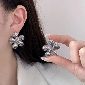 Vue détaillée des boucles d'oreilles fleur argentée avec effet lave texturé sur l'oreille