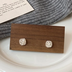 Macro shot of silver geometric earrings with pavé stones on a wooden display stand