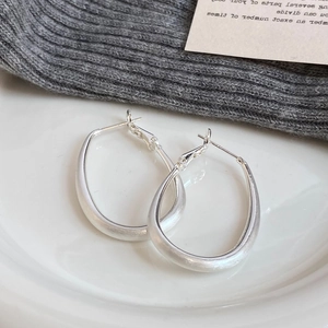 Minimalist silver matte brushed oval hoop earrings displayed on a white ceramic plate
