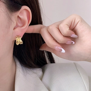 Golden irregular geometric C-shaped stud earrings worn by a model in a minimalist style