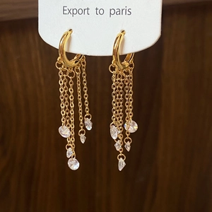 Detailed view of dangling gold tassel earrings with sparkling zircon crystals on white card