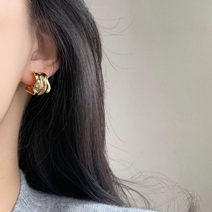 Minimalist gold plated C-shaped geometric ripple earrings worn by model on grey sweater