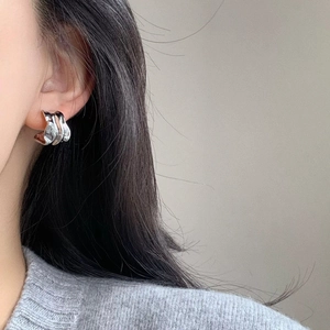 Macro shot of silver C-shaped earring with irregular pleated texture on a model