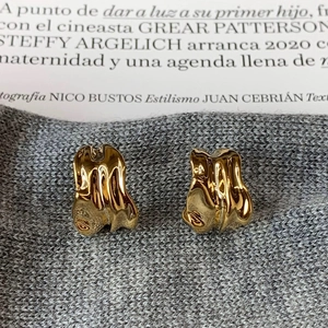 Macro shot of gold-plated irregular fluid earrings on a premium grey knit background