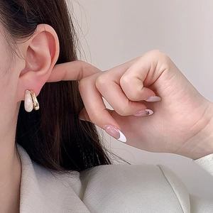 Detailed view of C-shaped gold-plated earrings with milky white enamel inlay on a model