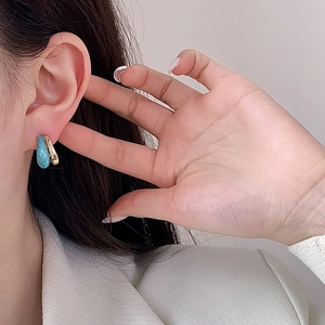 Two-tone C-shape earrings with gold plating and blue marble enamel on a model