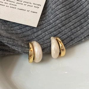 Detail of C-shaped gold plated earrings with white enamel on grey knit background