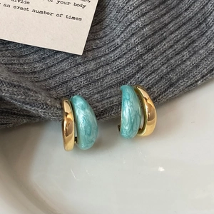 Gold-plated C-shaped earrings with marble-textured blue resin on a stylish fabric display