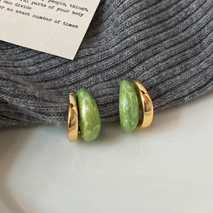Detailed macro view of gold-plated C-shaped earrings with green marbled enamel finish