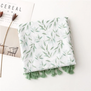 Detailed view of linen feel scarf featuring green leaf patterns and fringe tassels