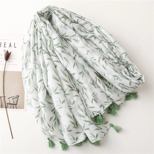 Elegant white cotton linen scarf with green leaf print and tassels on clean artistic background