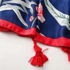 Macro detail of silk scarf showing deep blue floral print and red tassel craftsmanship