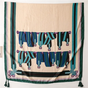 Détail de foulard en soie avec imprimé chaîne, base beige et glands verts sur bords