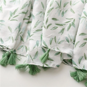 Detailed view of white linen scarf featuring green leaf print and matching fringe tassels