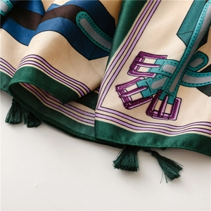 Gros plan d'un foulard en soie avec motifs de ceintures et glands vert foncé