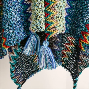 Close-up of bohemian knit shawl with colorful wavy patterns and blue tassel details