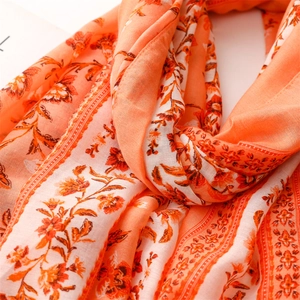 Detailed close-up of soft coral orange linen-feel scarf with elegant camellia floral pattern
