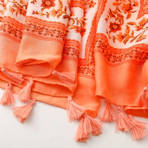 Macro detail of orange and beige cotton linen scarf with floral print and fringe tassels
