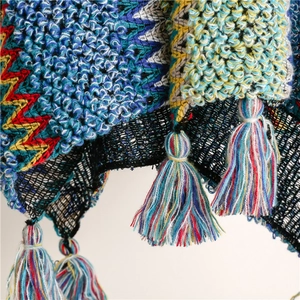 Macro shot of ethnic knit shawl featuring colorful tassel fringe and bohemian textures