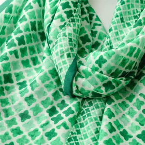 Detail of soft linen-touch scarf featuring green geometric patterns and tassel edges