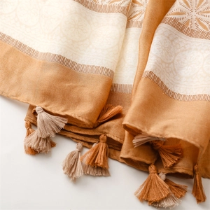 Detail of bohemian scarf with tassels and geometric patterns in warm ginger and white